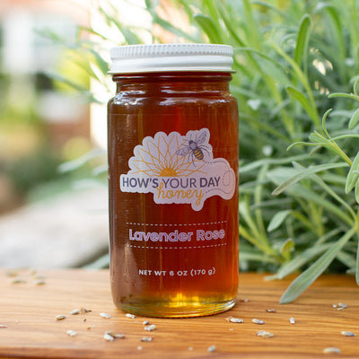 Raw local lavender rose infused honey from How's Your Day Honey in St. Petersburg FL, one 6oz jar. Photographed on a cutting board with lavender flowers..